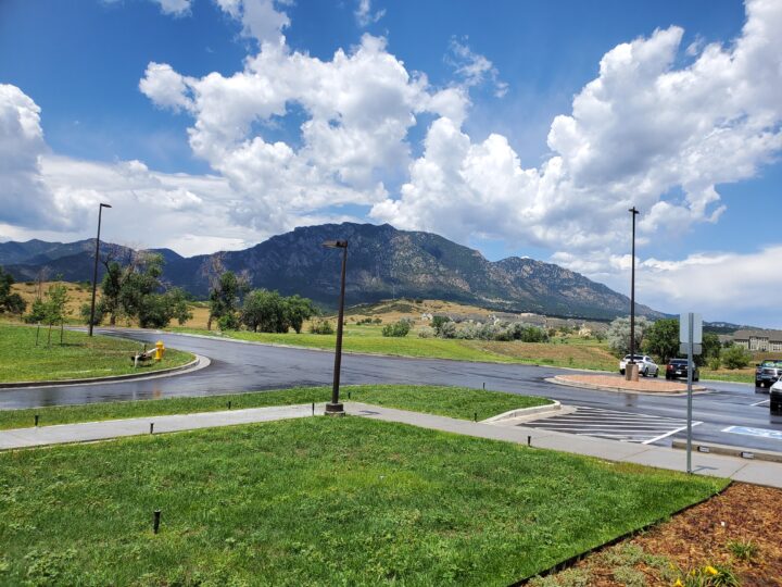 View outside from the medical center. Mountains are in the distance with clouds, grass, and a parking lot. 